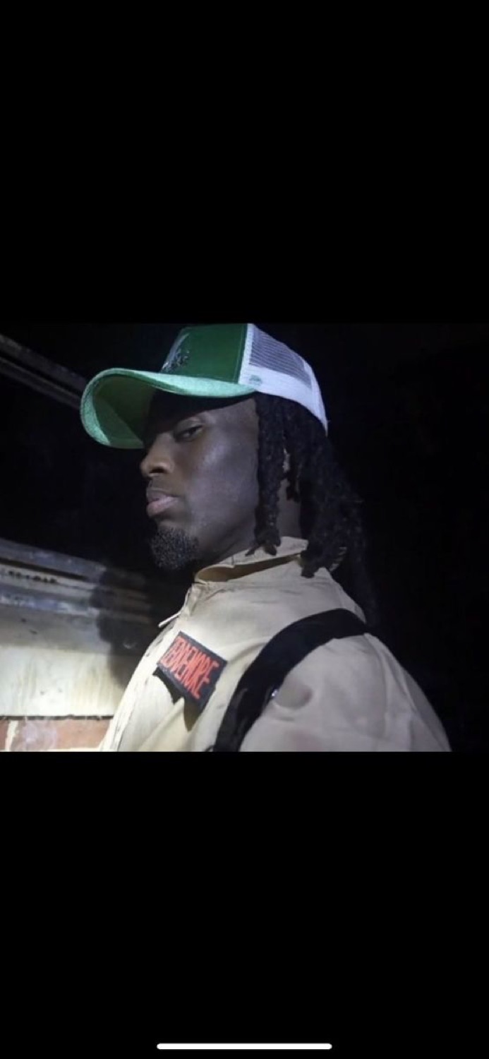Man in a green trucker cap looking off to the side with a cool deadpan stare