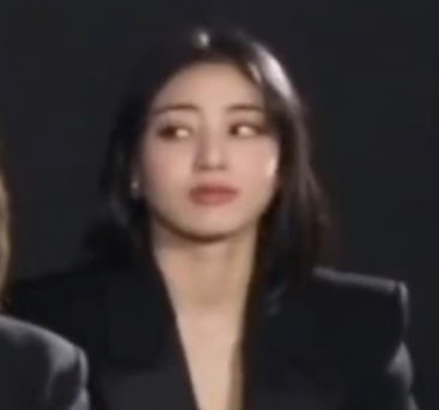 Young woman in black blazer glancing sideways with utterly cold, disinterested eyes