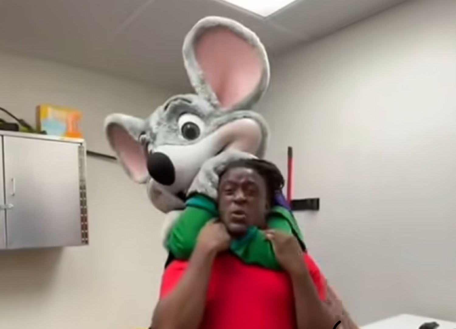 Man in a headlock from a giant mouse mascot, face frozen in panic