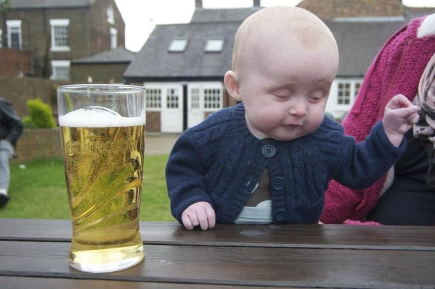 Bald baby at a pub table staring intensely at a full pint of lager like it's his next move