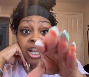Woman with bedazzled nails pointing at the camera with an intense, wide-eyed accusatory look