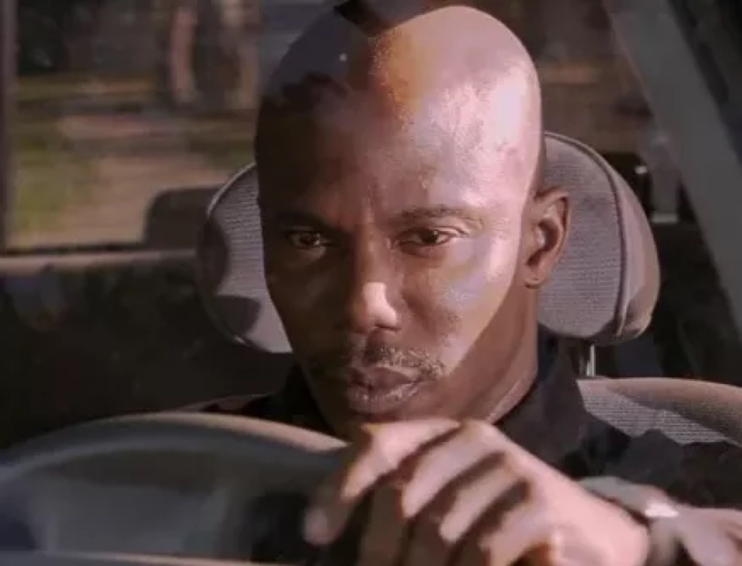 Bald man in a car driving with a flat, checked-out deadpan stare