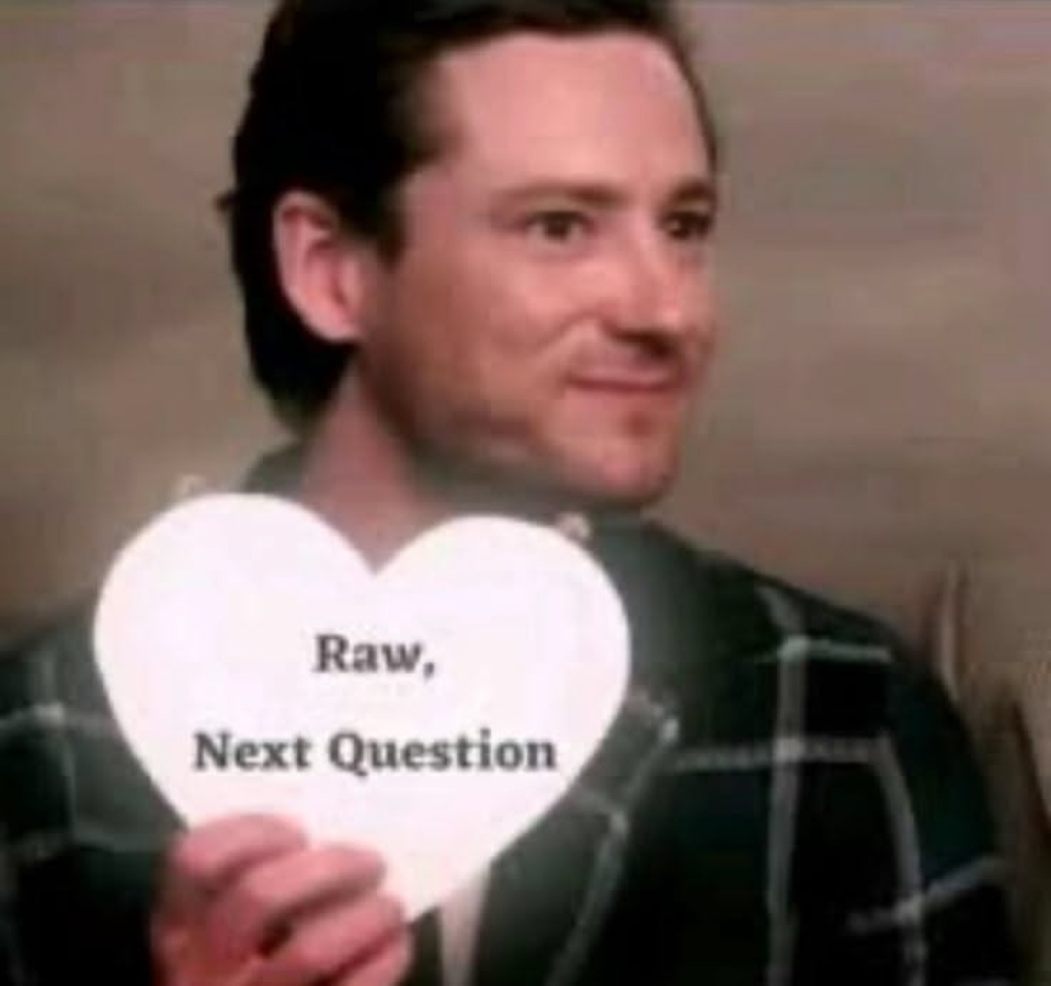 Man smirking behind a heart card reading 'Raw, Next Question', totally unbothered