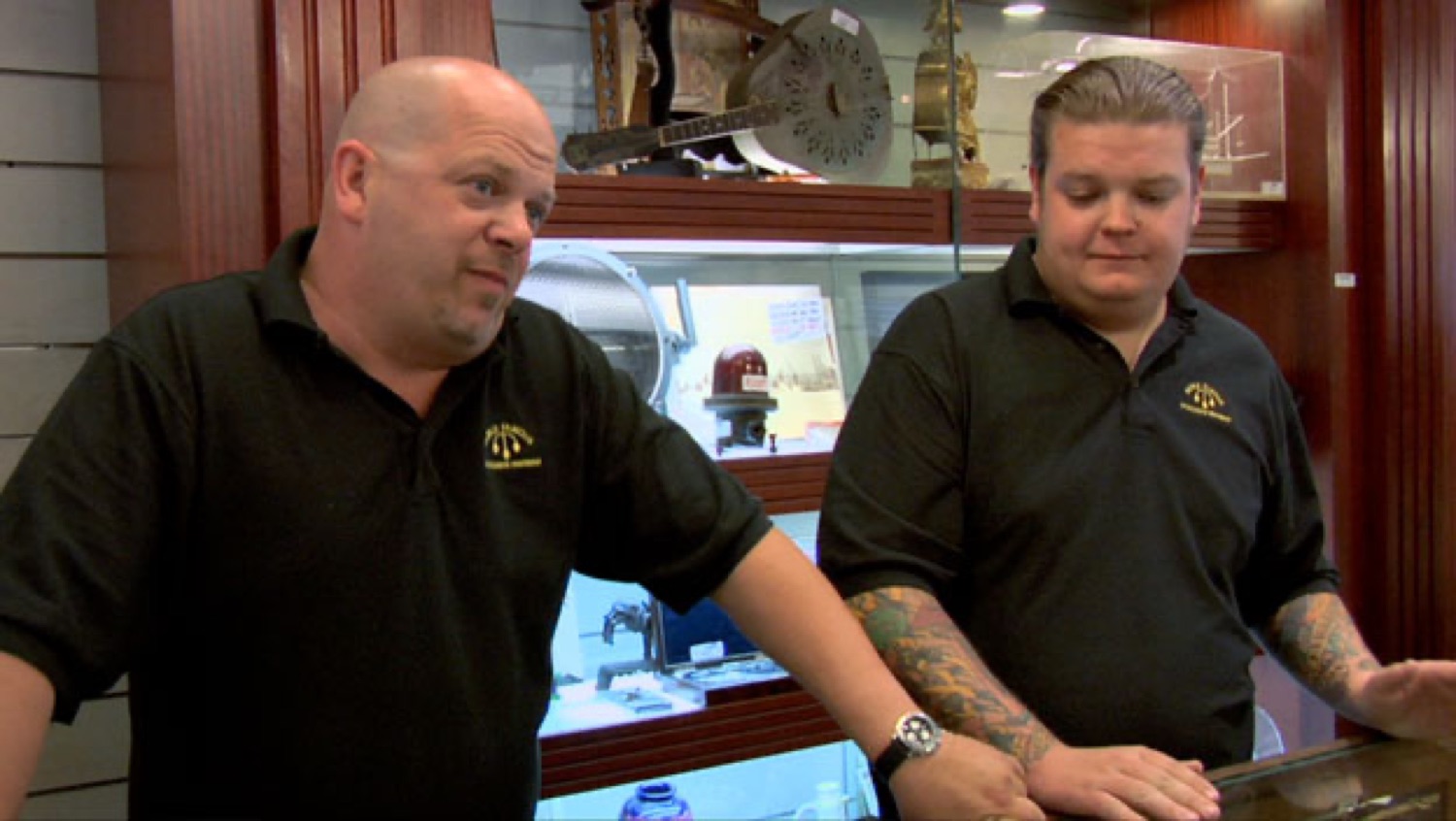 Two Pawn Stars guys behind the counter, one shooting a skeptical sideways look