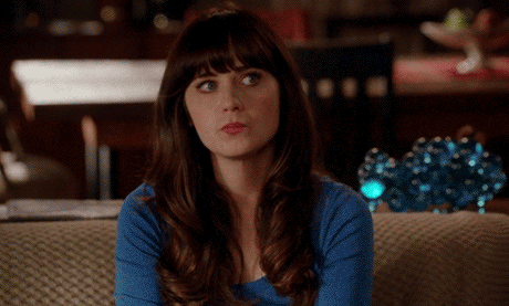Zooey Deschanel sitting on a couch giving an awkward, unimpressed side glance