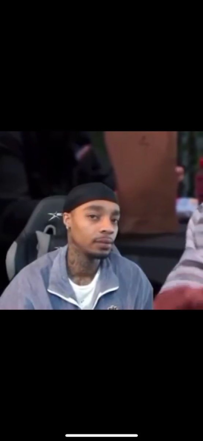 Guy in a durag sitting in a crowd with a flat, checked-out stare