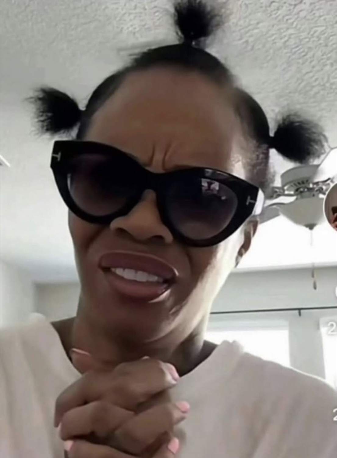 Woman in sunglasses with puff buns and clenched hands looking like she's desperately hoping for something