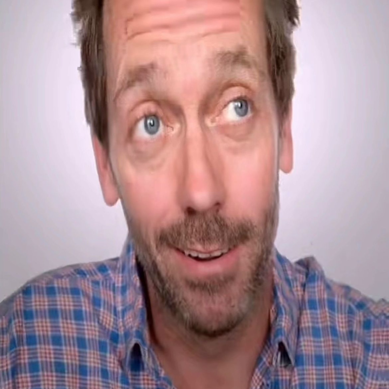 Hugh Laurie looking up with wide eyes and a slightly open mouth like he just heard the news
