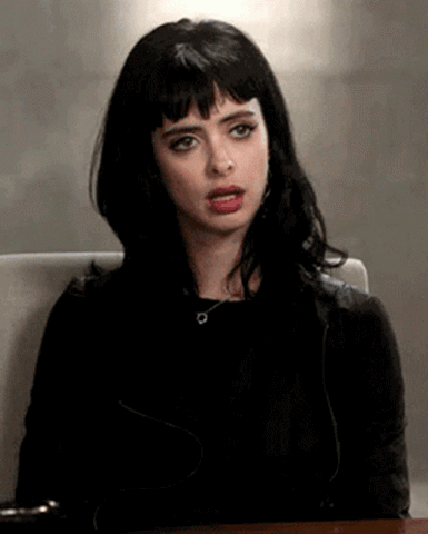 Dark-haired woman sitting with a flat, unimpressed and done-with-it look