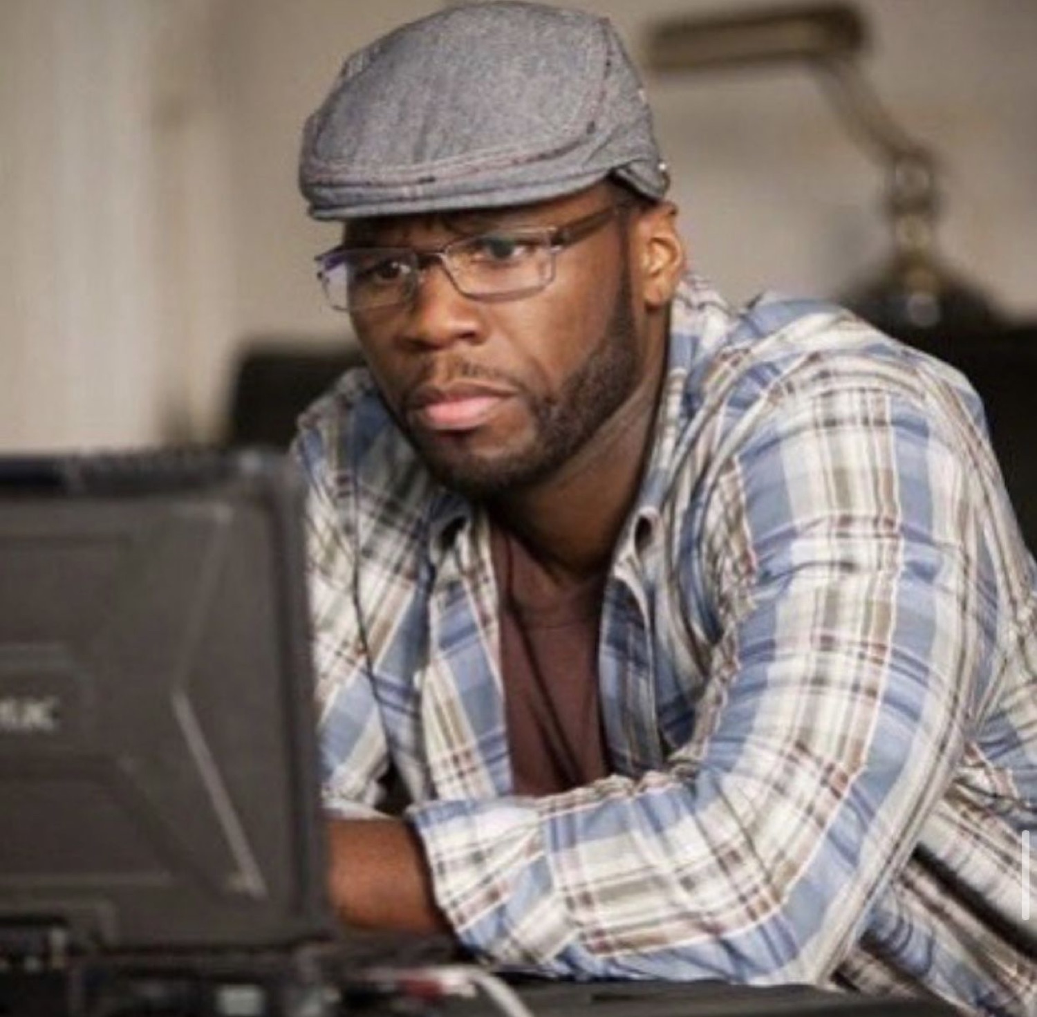 Man in a flat cap and glasses leaning over a laptop with a skeptical, judging look