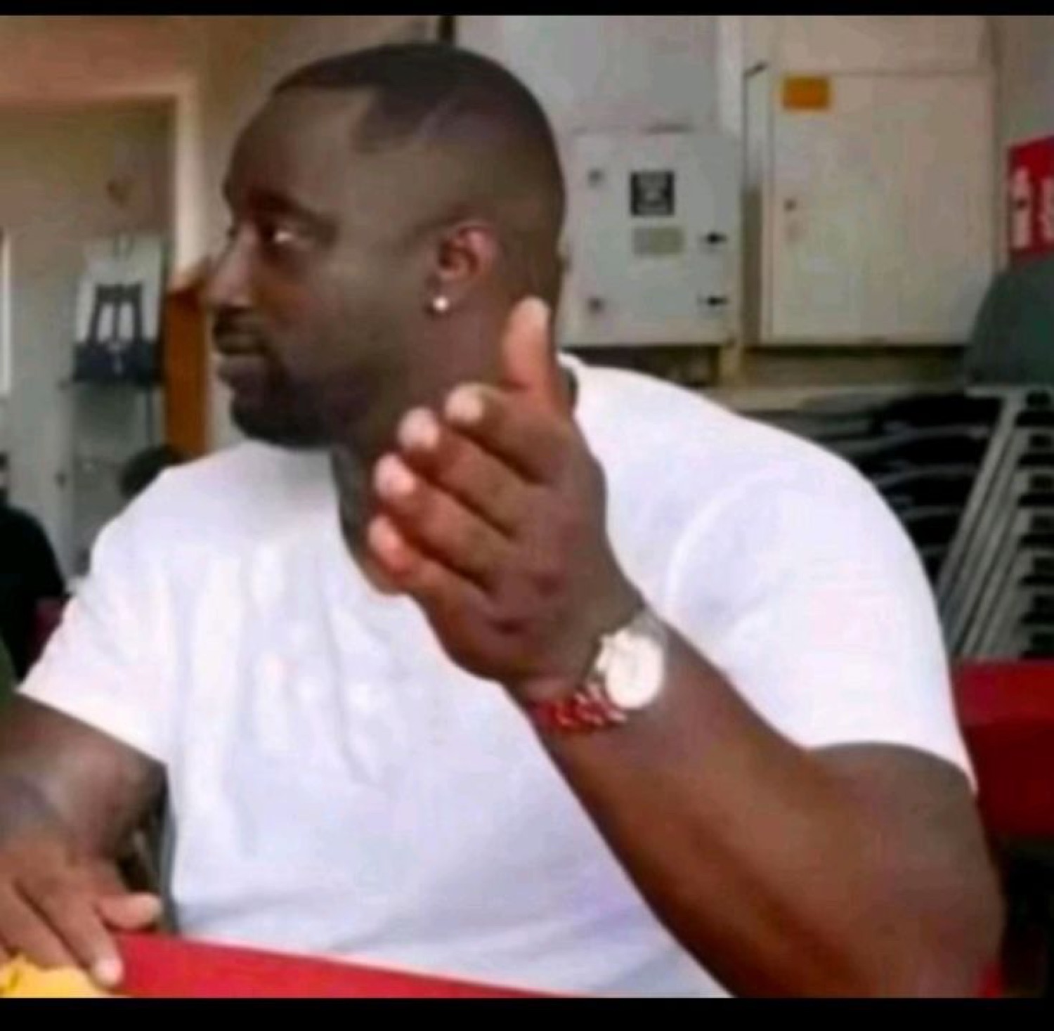 Man in a white tee sitting sideways and stroking his chin, deep in scheming thought