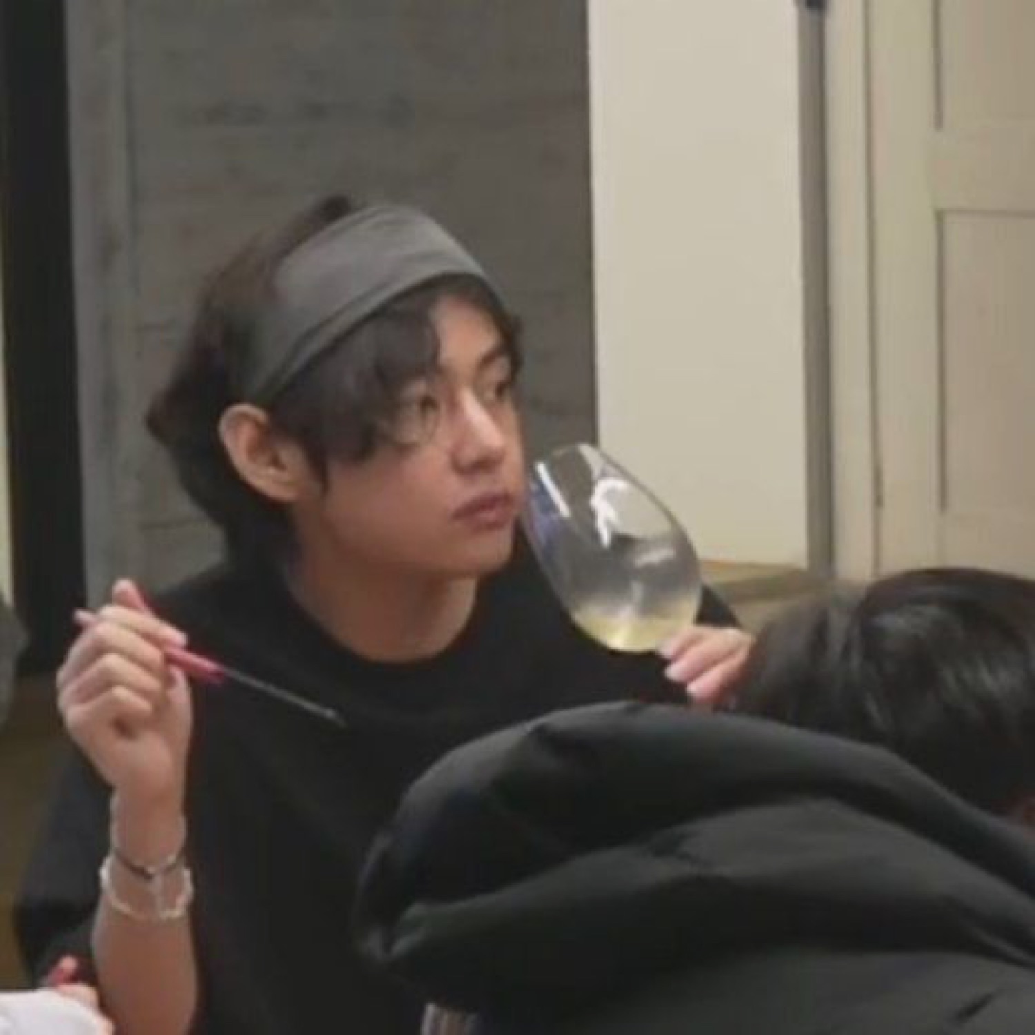 Guy in a headband sipping wine while shooting a sidelong glance