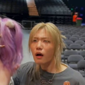 Blond-haired person in an empty arena, mouth open in stunned disbelief