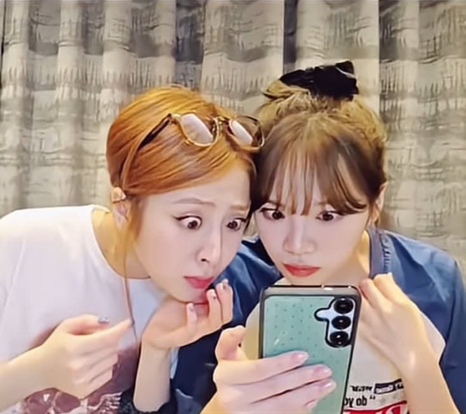 Two young women leaning together, staring wide-eyed at a phone screen with alarm