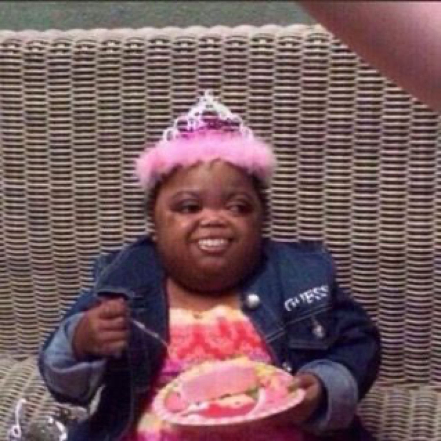 Woman in a pink tiara grinning while digging into a slice of birthday cake