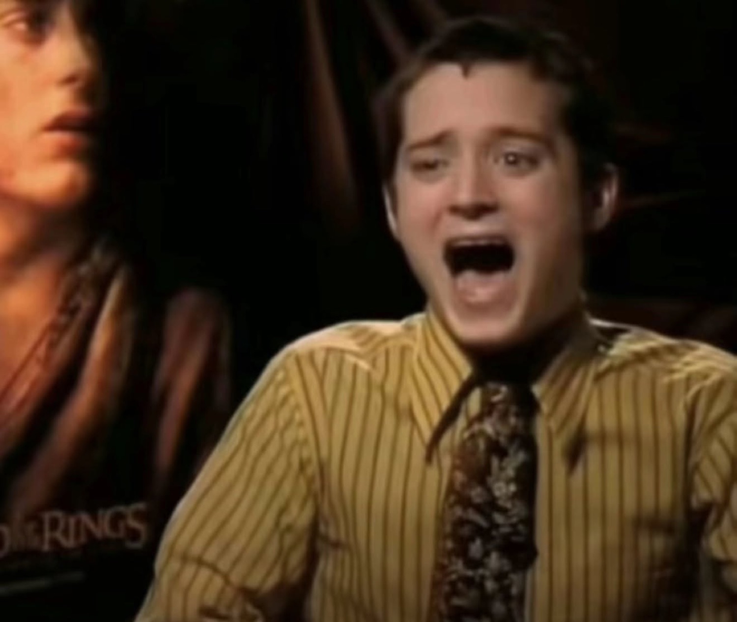 Elijah Wood screaming with mouth wide open in front of a Lord of the Rings poster
