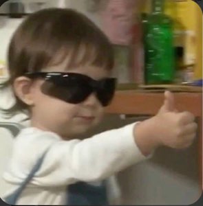 Toddler in sunglasses giving a confident thumbs up