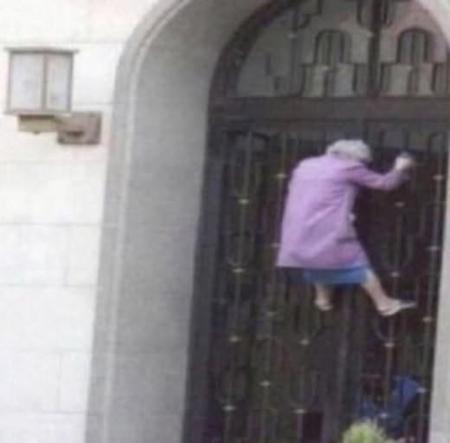 Old woman in a purple coat climbing over a wrought-iron gate to escape