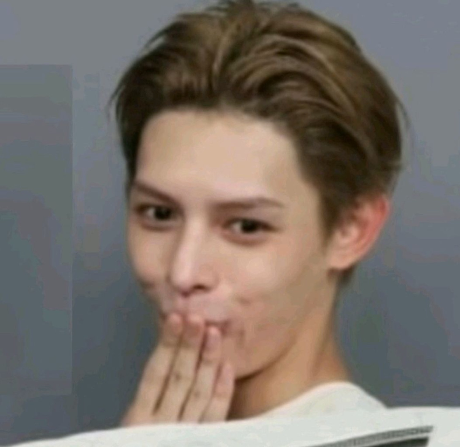 Young East Asian man covering his mouth with his hand and giving a sly sideways smile