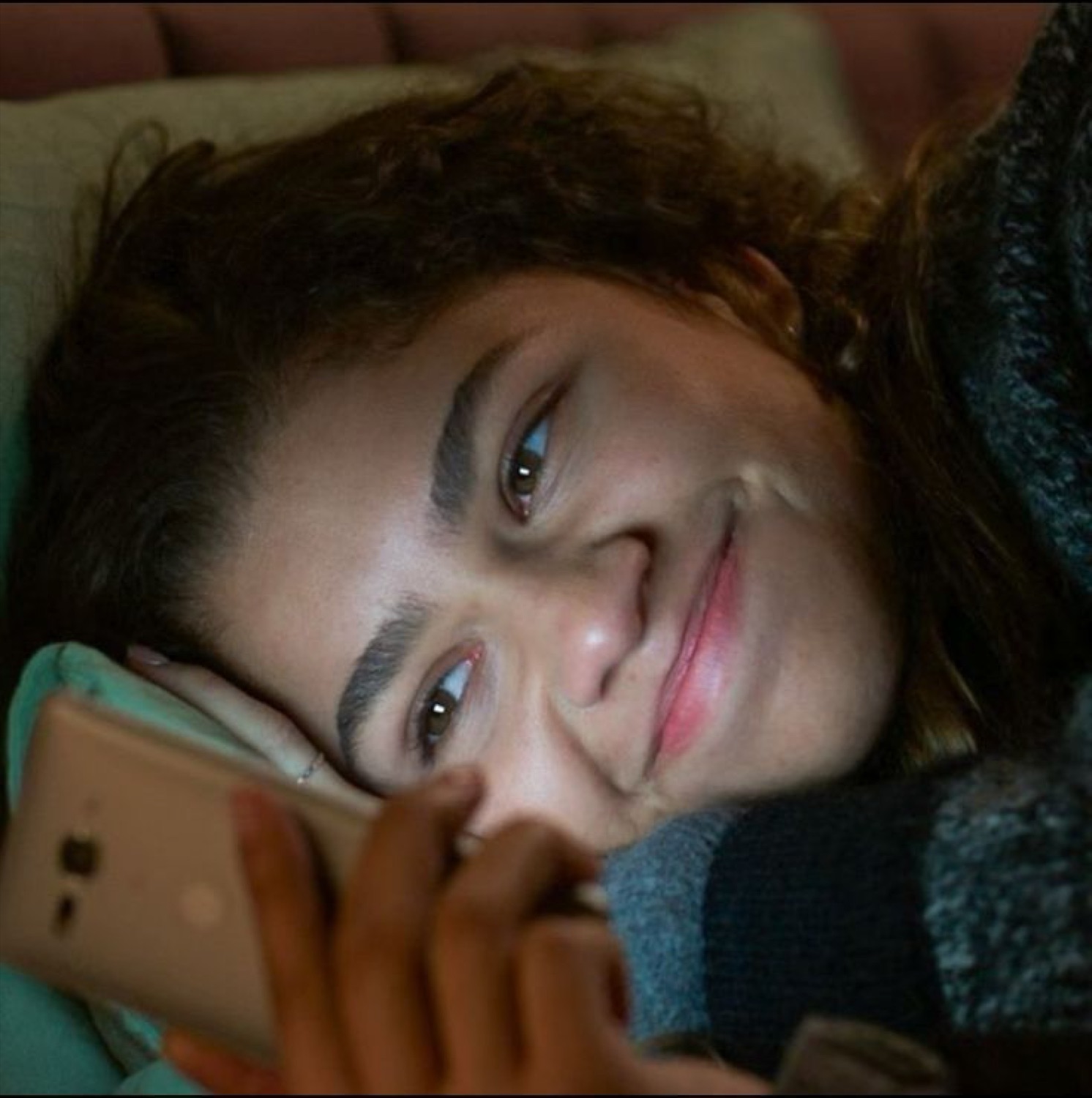 Woman lying in bed smiling softly at whatever just lit up her phone