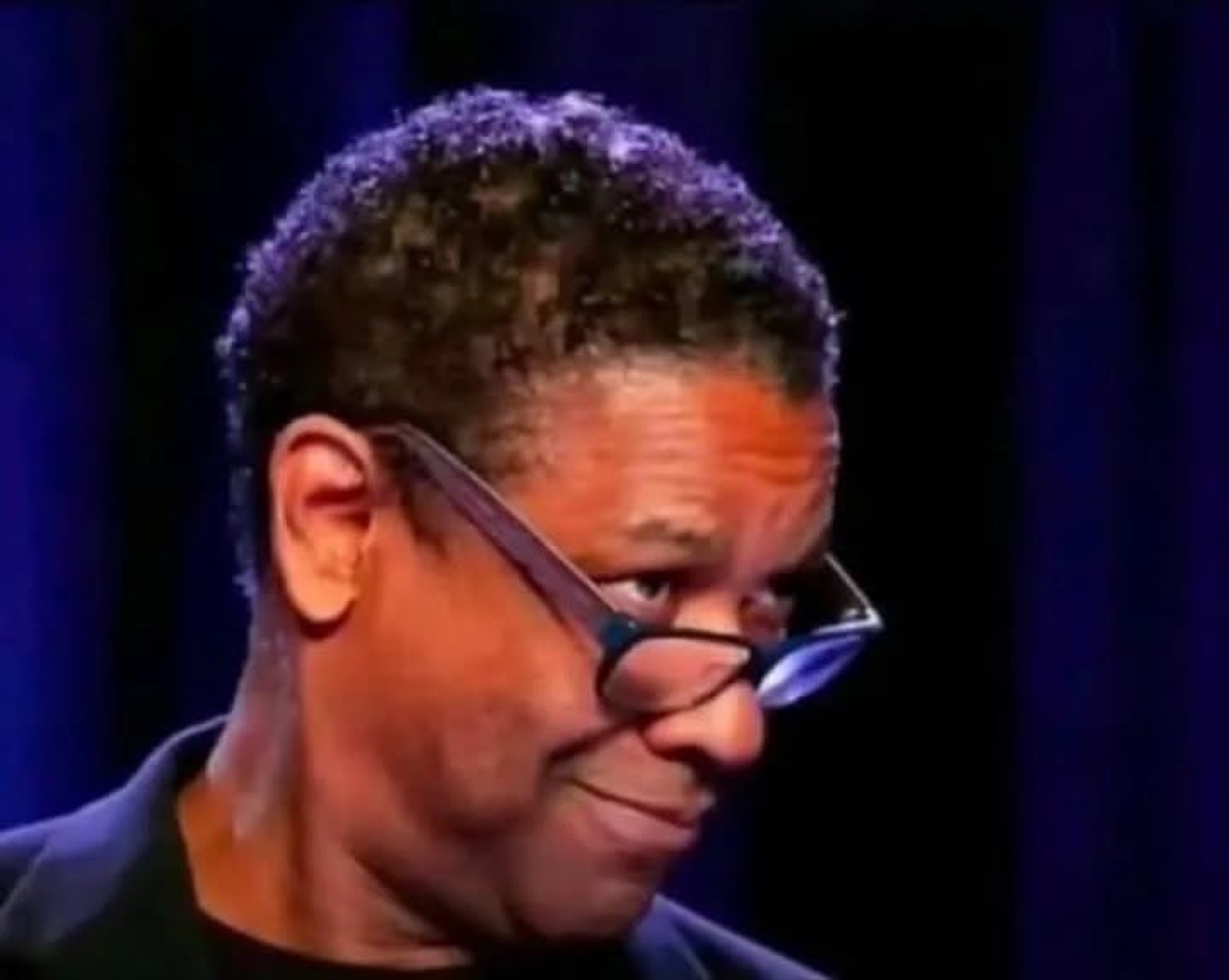 Denzel Washington peering over his glasses with a slow, knowing smirk