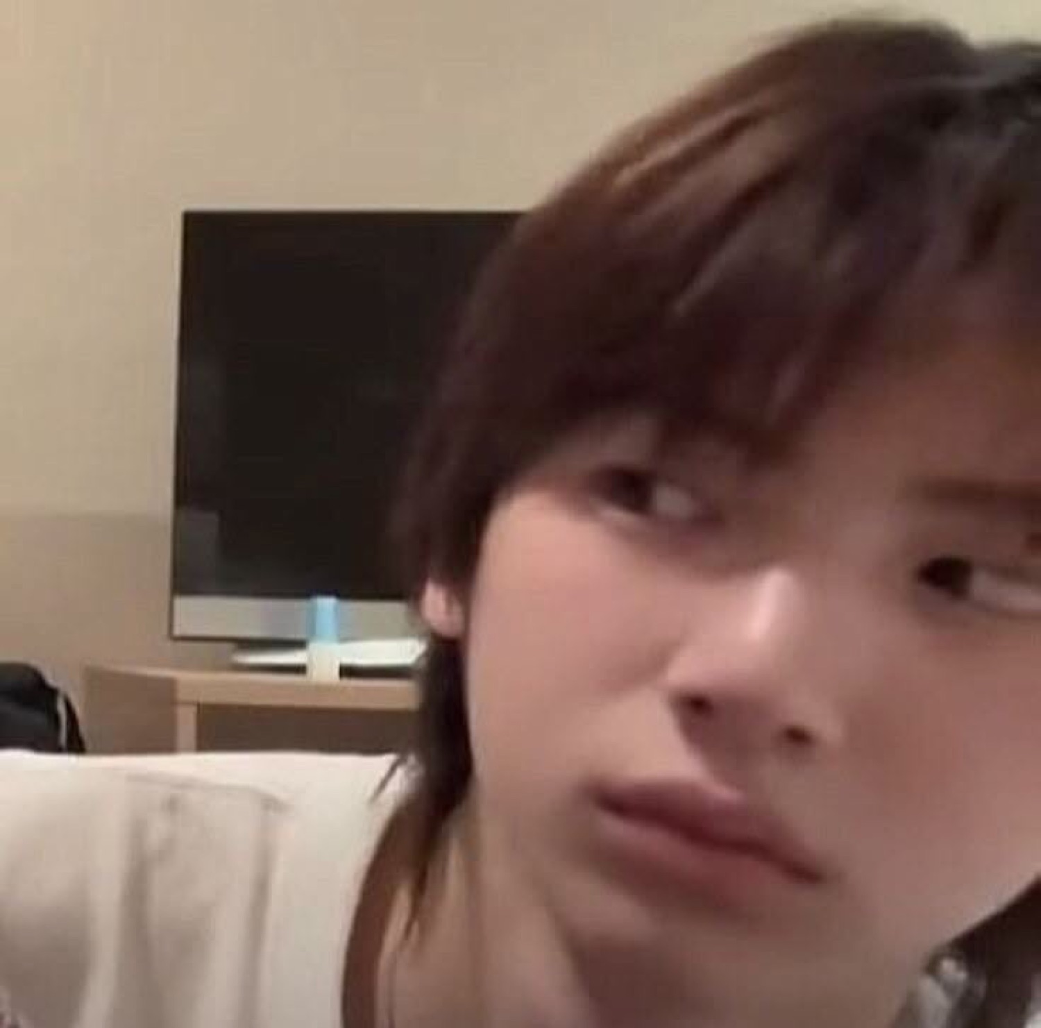 Person leaning into the camera giving a flat, annoyed side-eye in a bedroom