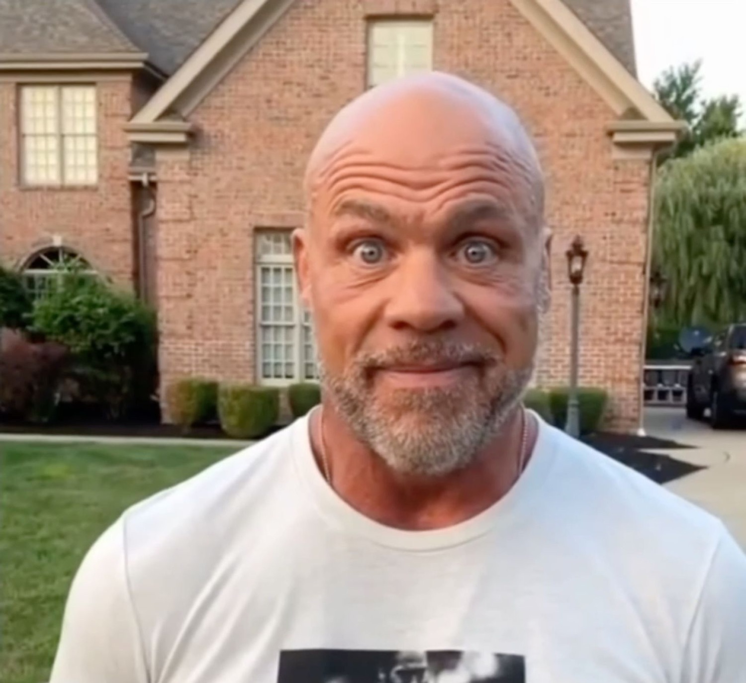 Bald man in a white tee outside a house with a wide-eyed startled look