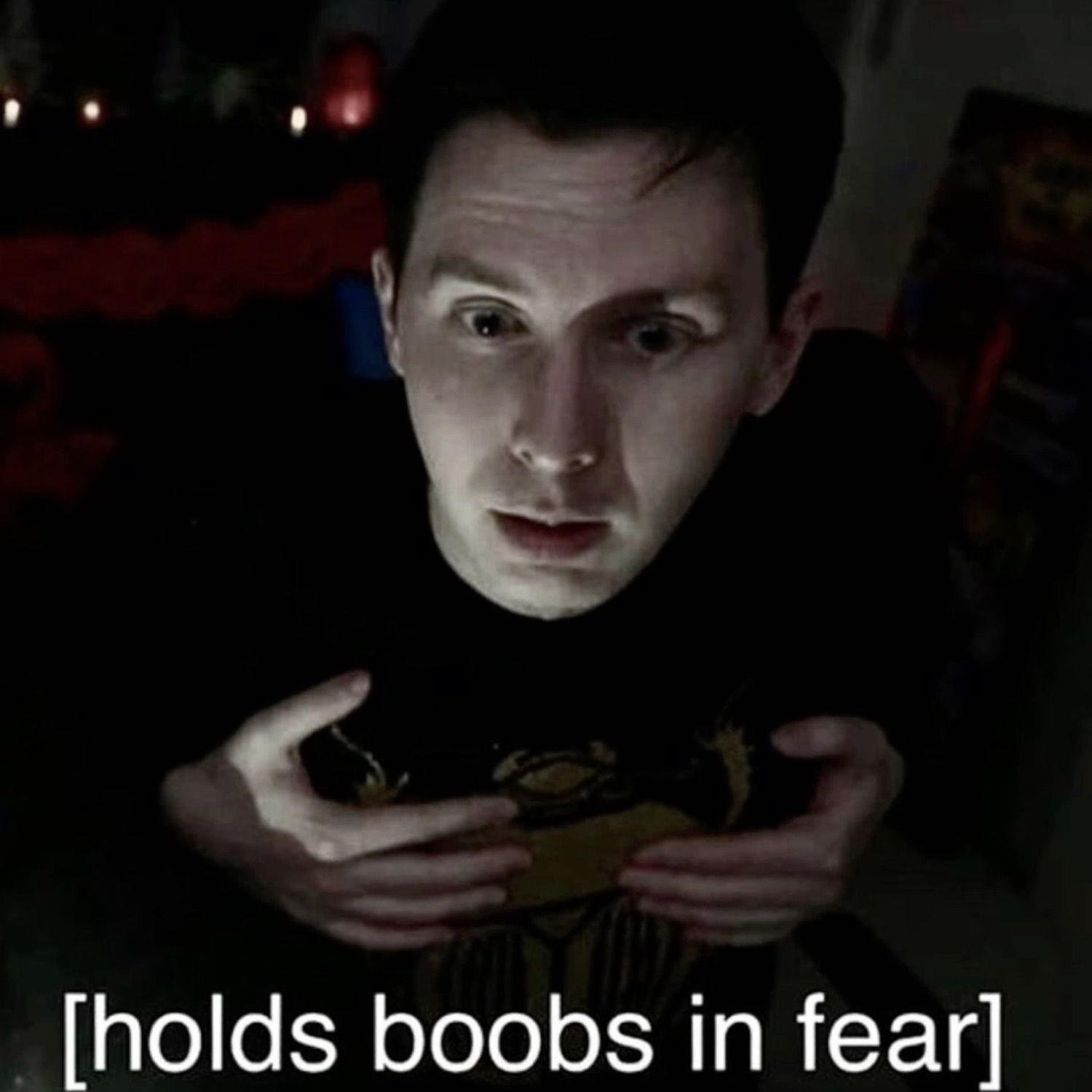 Man in a dark room clutching his chest wide-eyed, captioned '[holds boobs in fear]'