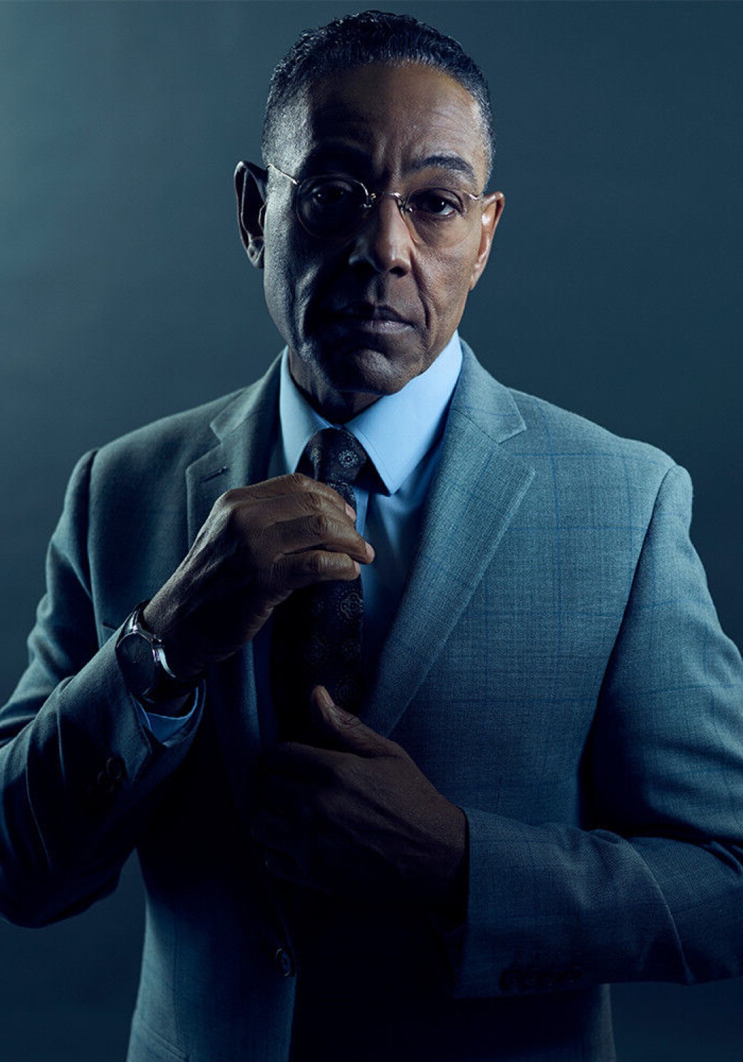 Gus Fring in a grey suit calmly adjusting his tie with a cold, level stare