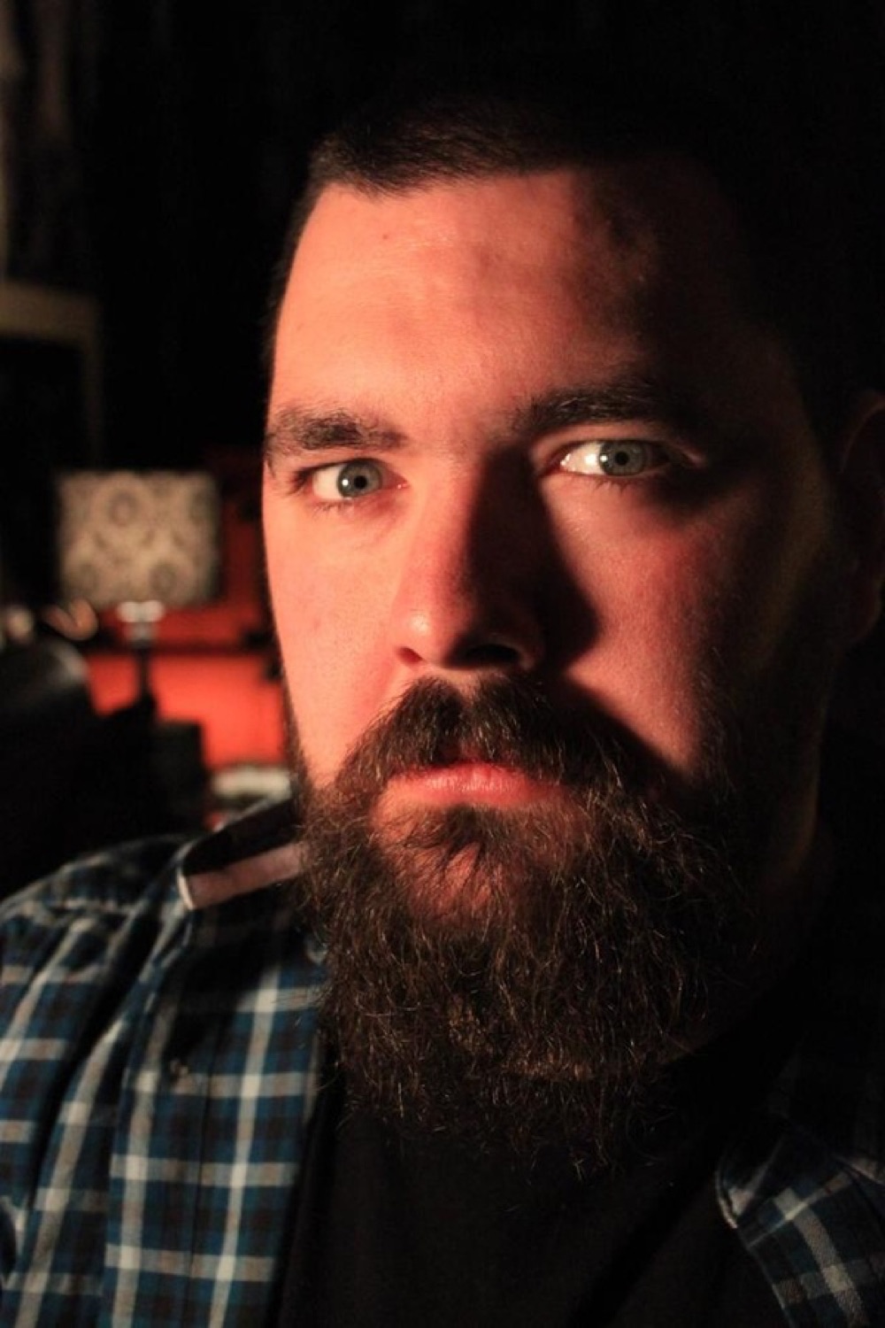 Bearded man with piercing blue eyes staring intensely from a dark, dramatically lit photo