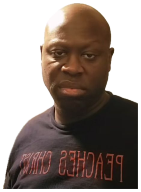 Bald man in a Peaches Christ shirt staring into the camera next to a microwave with zero emotion sticker